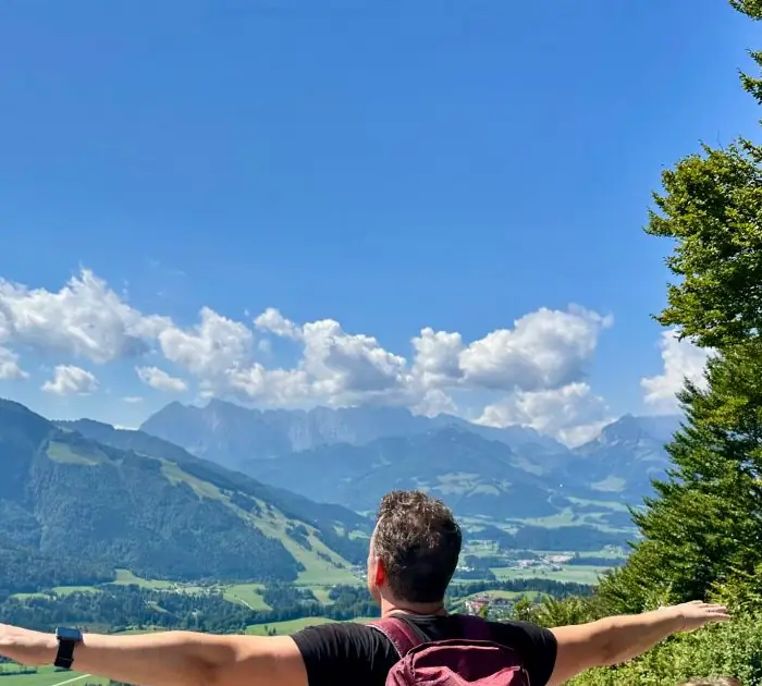 Wanderer breitet oben am Aussichtspunkt die Arme vor dem Alpenpanorama aus