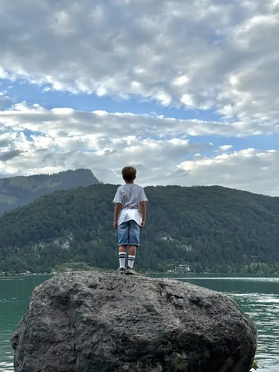 Kind steht abends auf einem Felsen am Ufer des Walchsees