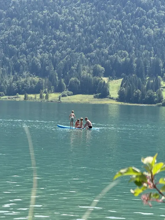 Stand-up-Paddler auf dem türkisen Walchsee vor bewaldeten Hängen